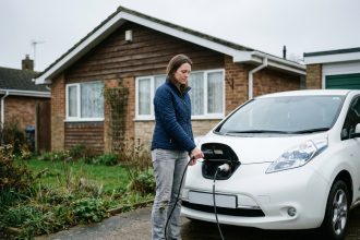 Femme branchant le câble de recharge d'une Nissan Leaf blanche dans une allée résidentielle