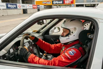 Pilote en combinaison de course rouge assis dans le cockpit d'une voiture de sport sur un circuit automobile professionnel