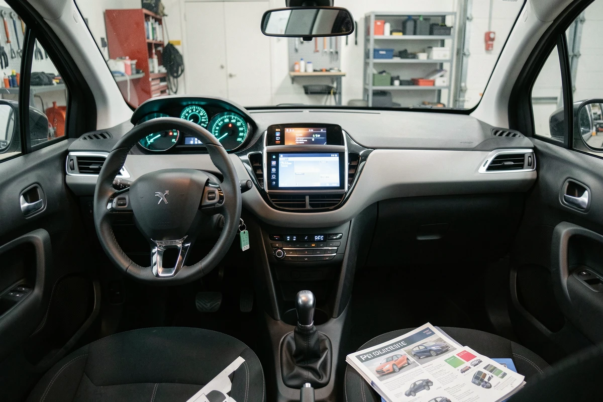 Vue complète du tableau de bord d'une Peugeot 208 avec éclairage ambiant personnalisé en bleu-vert dans un garage moderne